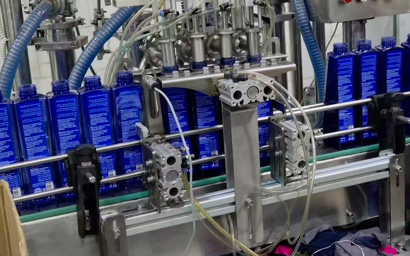 Four-nozzle filling station dispensing shampoo into blue bottles on a conveyor