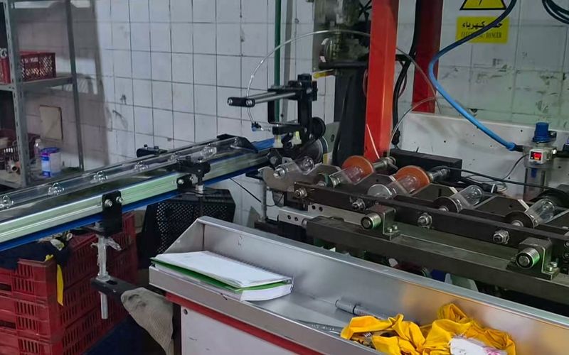 Bottle printing machine with a conveyor and roller fixtures holding clear bottles