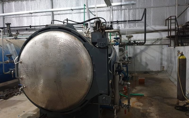 Horizontal olive sterilization autoclave with a round stainless-steel door in a processing hall