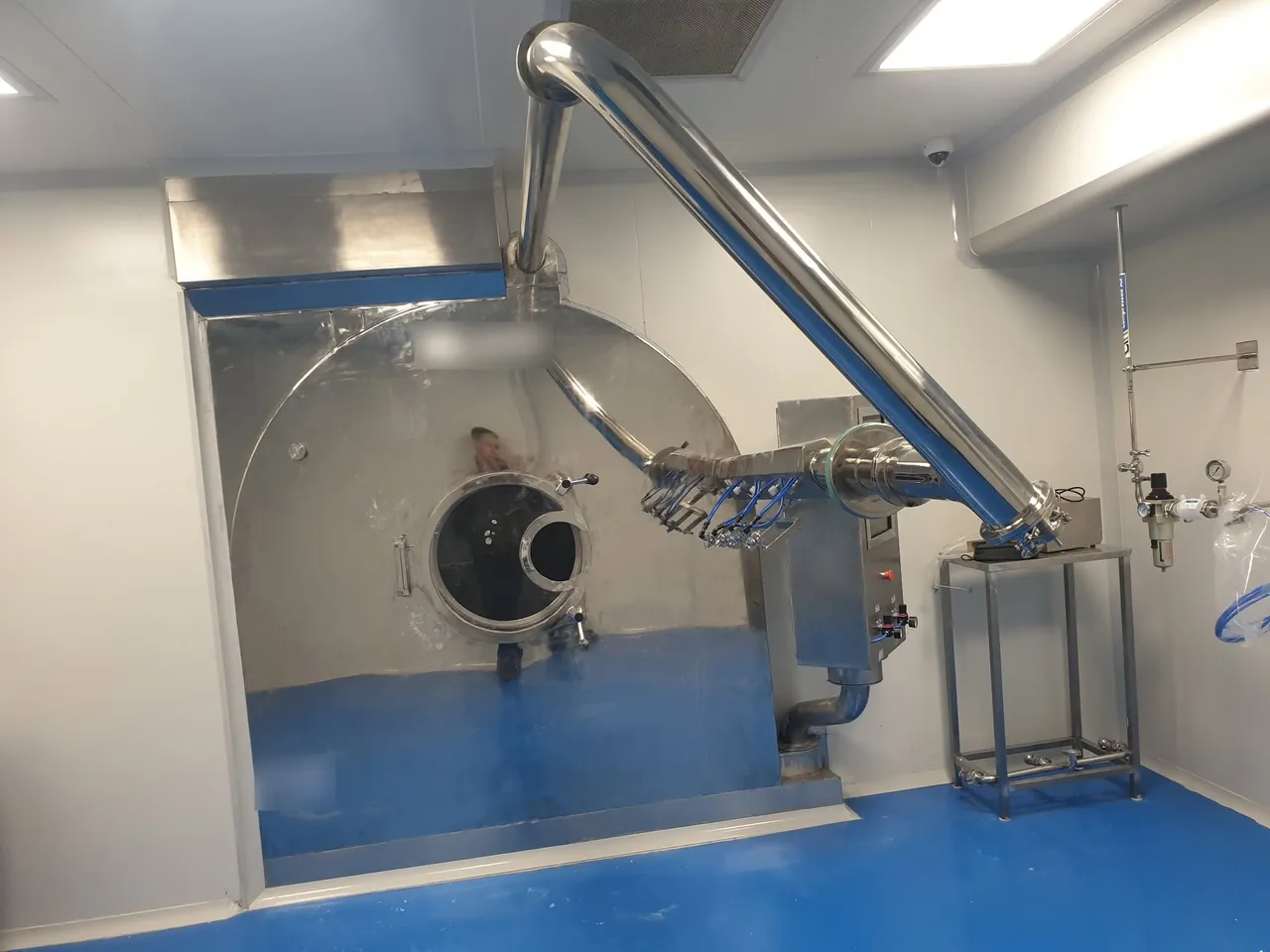Stainless-steel tablet coating drum with spray-gun arm and exhaust duct in a pharmaceutical cleanroom
