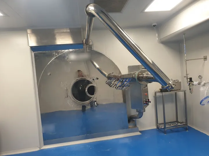 Stainless-steel tablet coating drum with spray-gun arm and exhaust duct in a pharmaceutical cleanroom